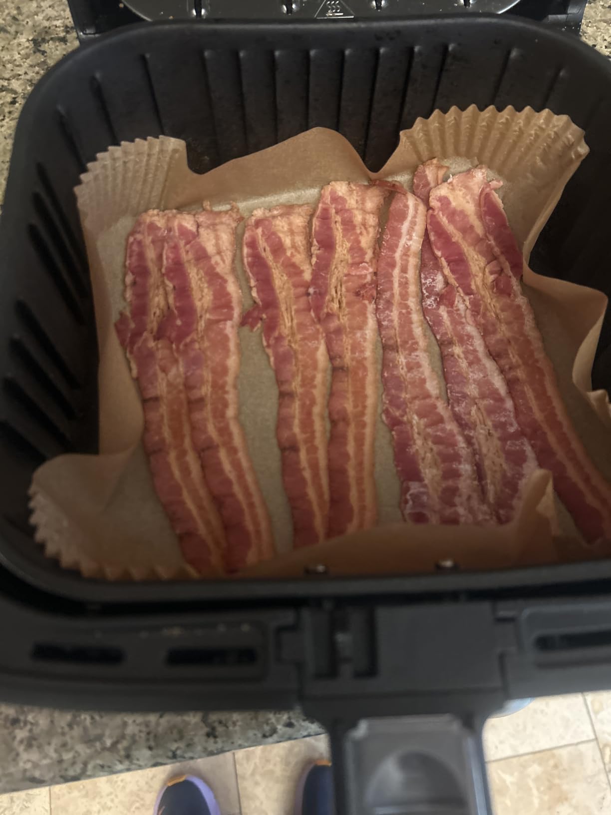 Raw bacon strips arranged on parchment paper inside an air fryer basket