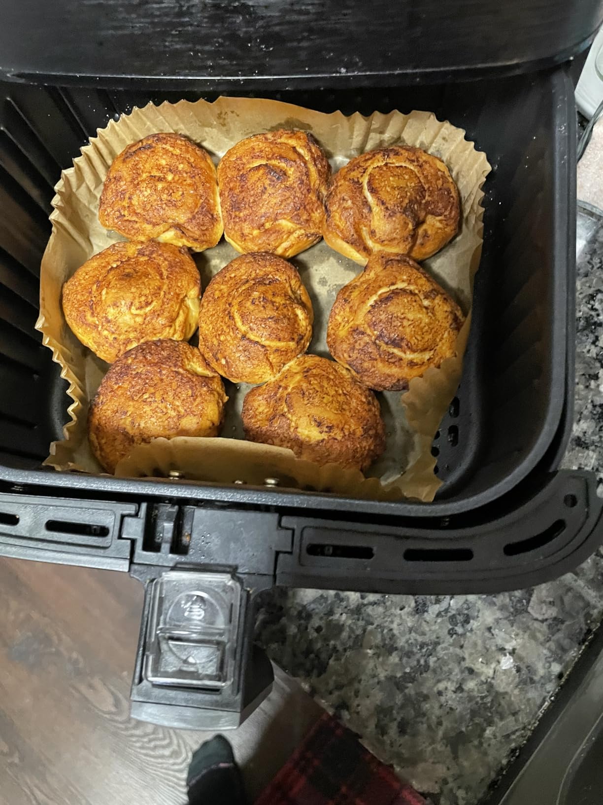 Golden brown baked rolls inside an air fryer basket on parchment paper