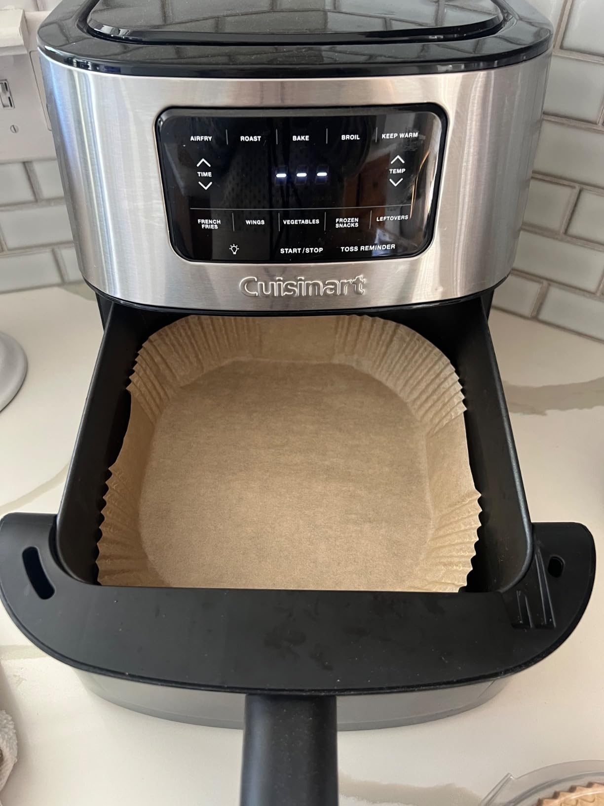 Cuisinart air fryer with a square parchment paper liner inside the open basket