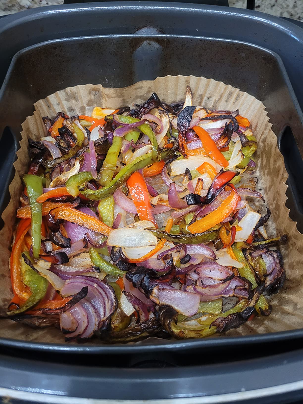 Sliced bell peppers and red onions roasted in an air fryer basket lined with parchment paper