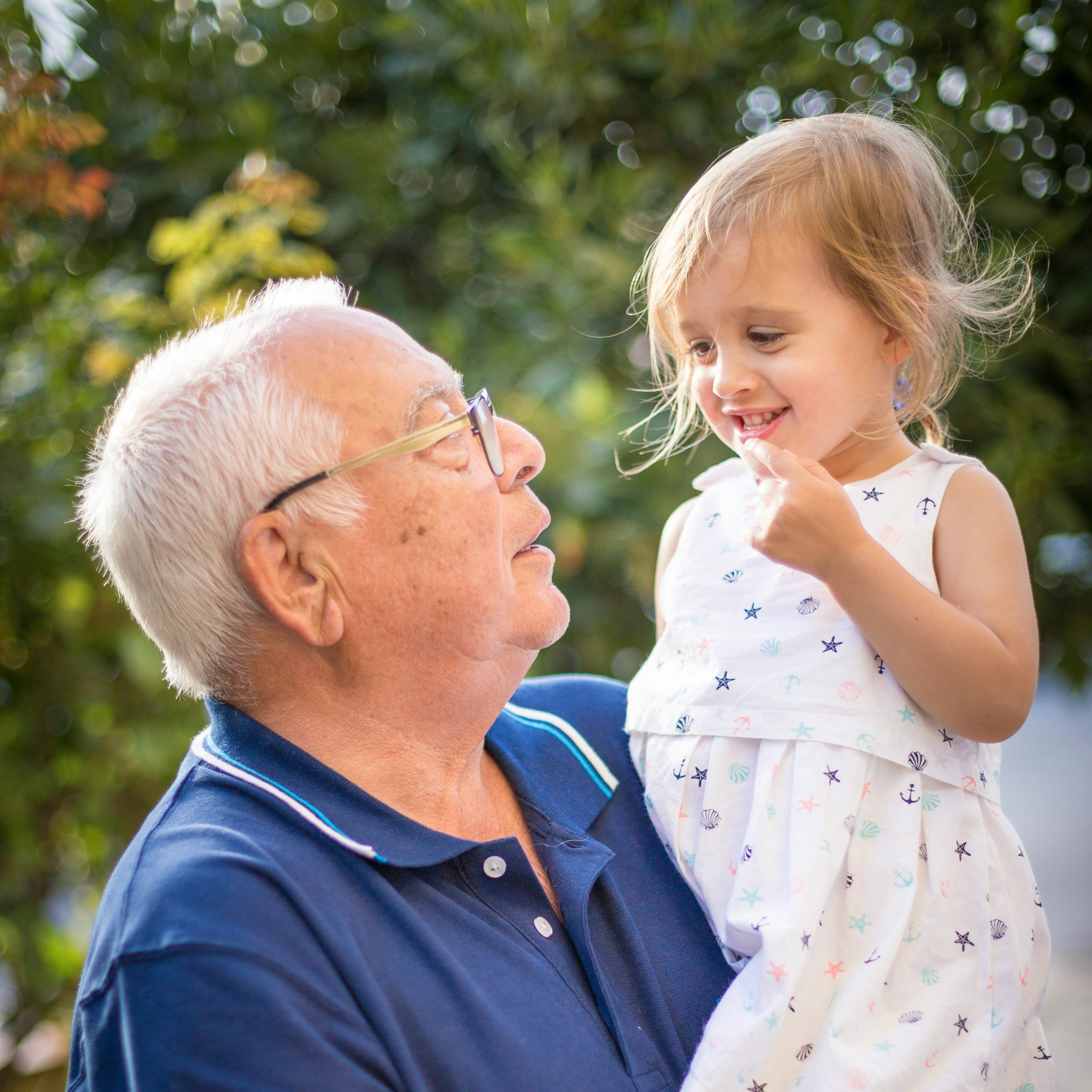 Elderly man in glasses holding a young girl in a white dress with nautical patterns